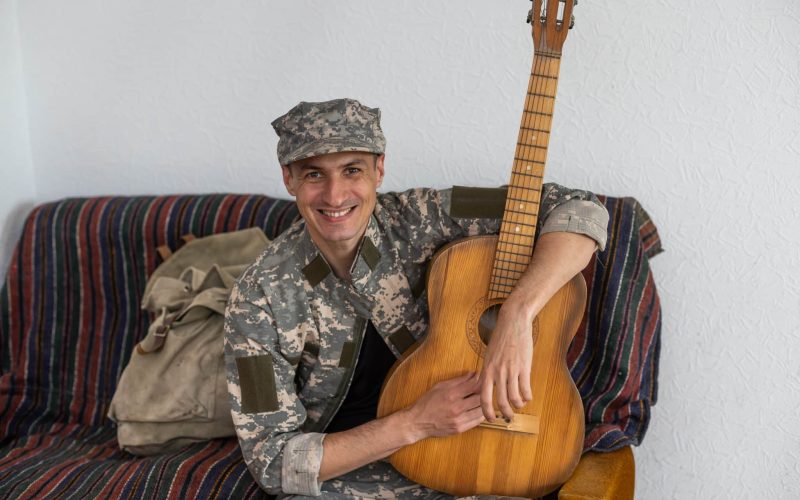 Veteran In The Wheelchair Guitar Play Concept. Family Meeting. Son And Wife. Camouflage Uniform. Family Background. Resting Together. Feelings Showing. Patriotic Comeback. Paralyzed Soldier
